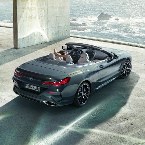 BMW M850i xDrive Кабриолет, с высоты птичьего полета. BMW M850i xDrive Кабриолет в Dravit Grey металлик с открытым мягким верхом, с высоты птичьего полета, парковка в бетонном здании перед океаном.
