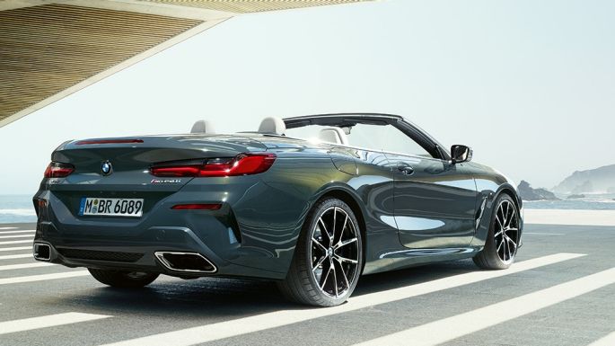 BMW M850i xDrive Кабриолет, вид сзади с поворотом в три четверти. BMW M850i xDrive Кабриолет в Dravit Grey металлик с открытым мягким верхом, вид сзади с поворотом в три четверти, парковка перед океаном.