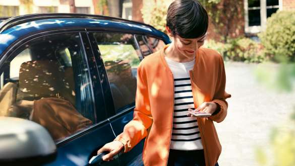 Женщина смотрит на свой смартфон и открывает дверь своего BMW BMW Teleservices, женщина смотрит на свой смартфон и открывает дверь своего BMW