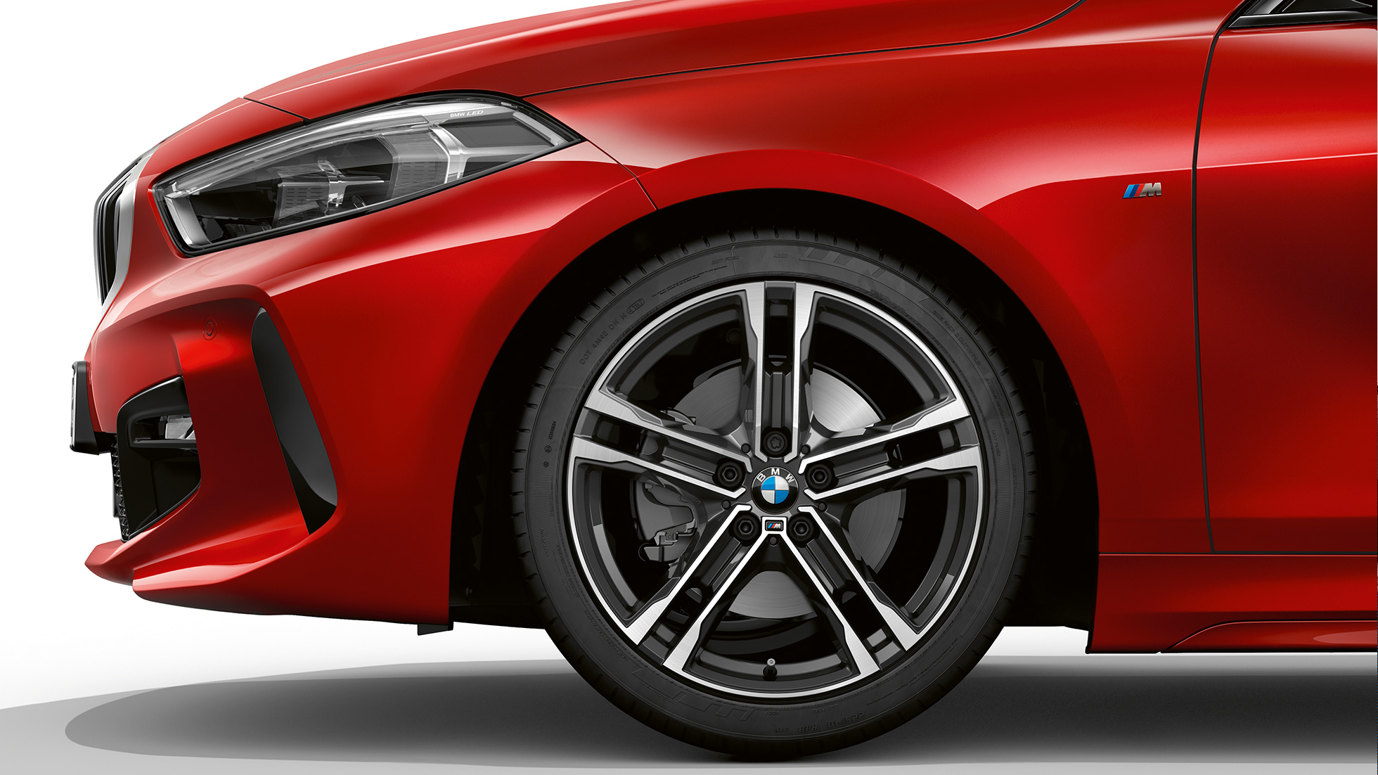 BMW 1 серии модель M Sport, спереди сбоку. BMW 1 серии модель M Sport в Melbourne Red металлик, спереди сбоку с 17-дюймовыми легкосплавными дисками M с двойными спицами, стиль 550 M, двухцветные.