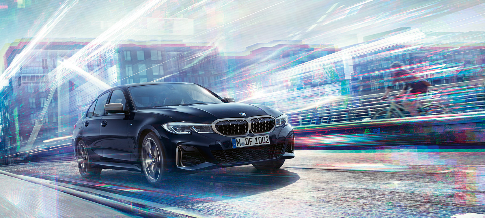 BMW 3 серии Седан, BMW M340i xDrive. Вид сбоку BMW M340i xDrive с поворотом в три четверти, едущего по дороге на фоне городских пейзажей.