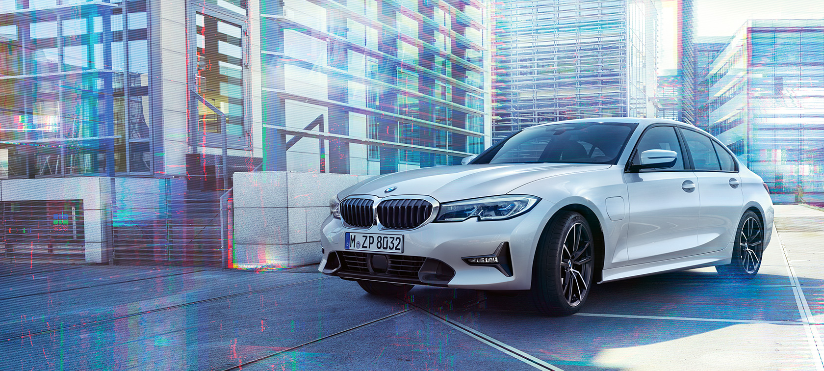 BMW 3 серии Седан 330e. Передний снимок седана BMW 3 серии 330е на городском фоне с поворотом в три четверти.