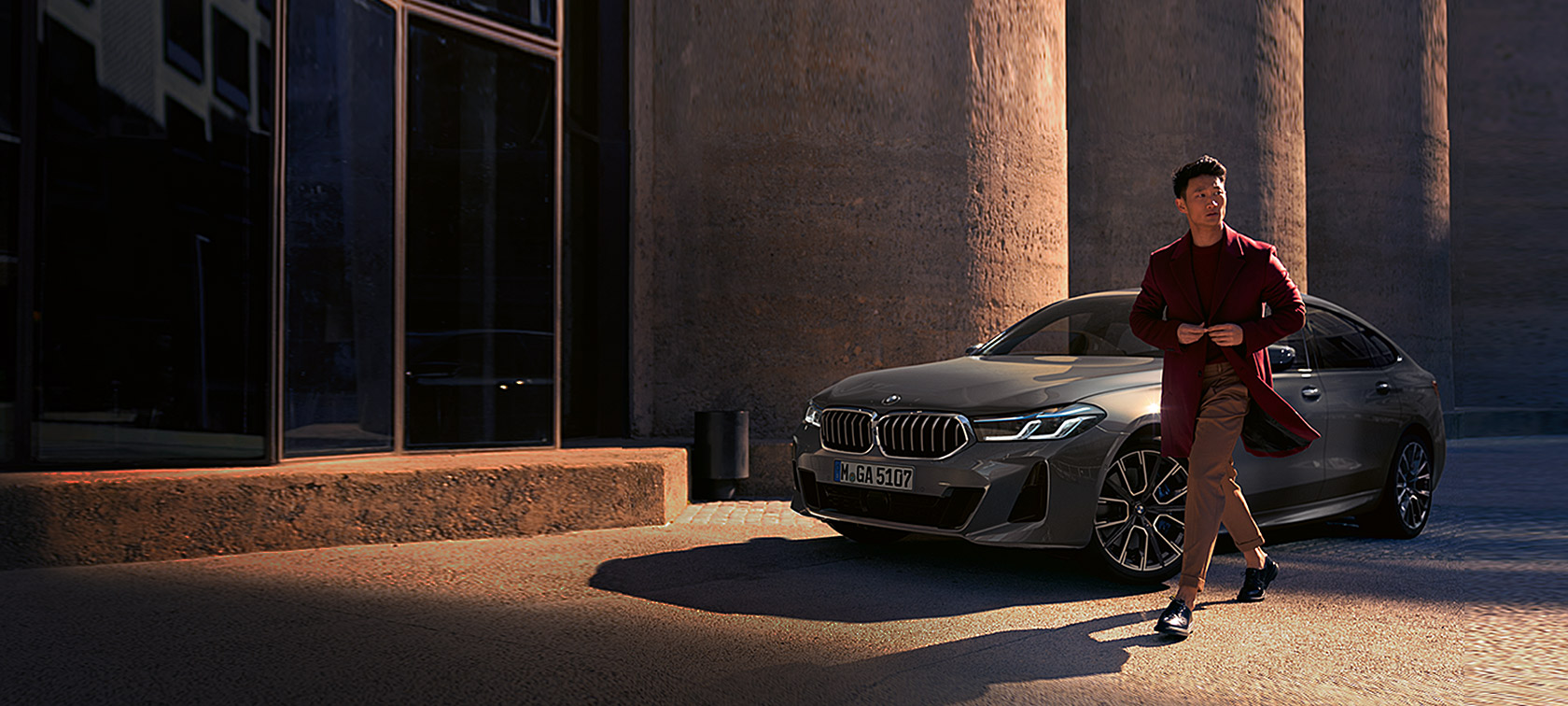 BMW 6-й серии Gran Turismo 640i xDrive G32 2020 года серого цвета Bernina Grey в неподвижном положении, вид спереди в три четверти, мужчина на фоне BMW