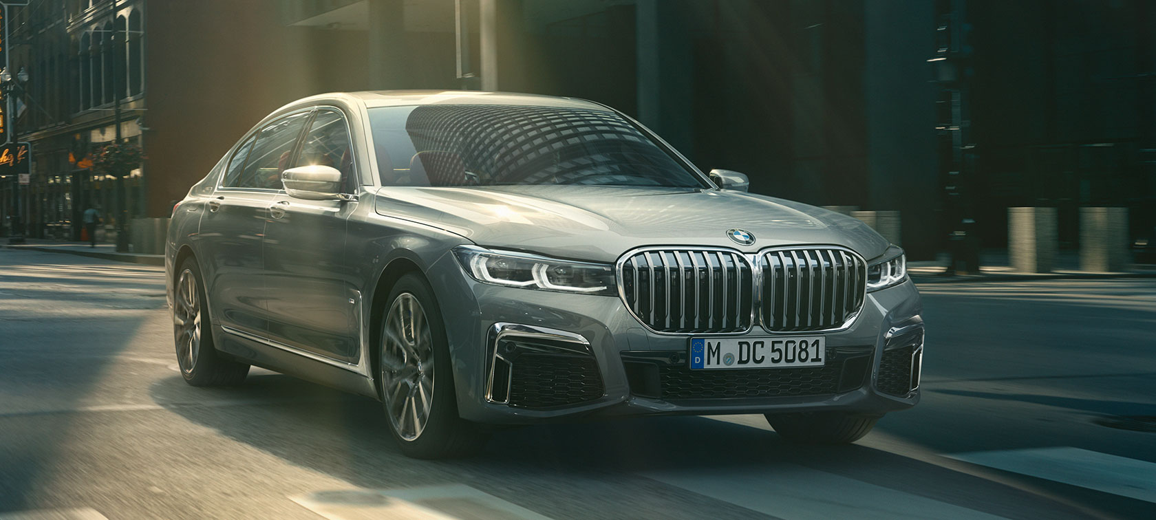 BMW 7 серии Седан серого цвета в движении по городским улицам: вид спереди с поворотом в три четверти BMW 7 серии Седан серого цвета в движении: вид спереди с поворотом в три четверти