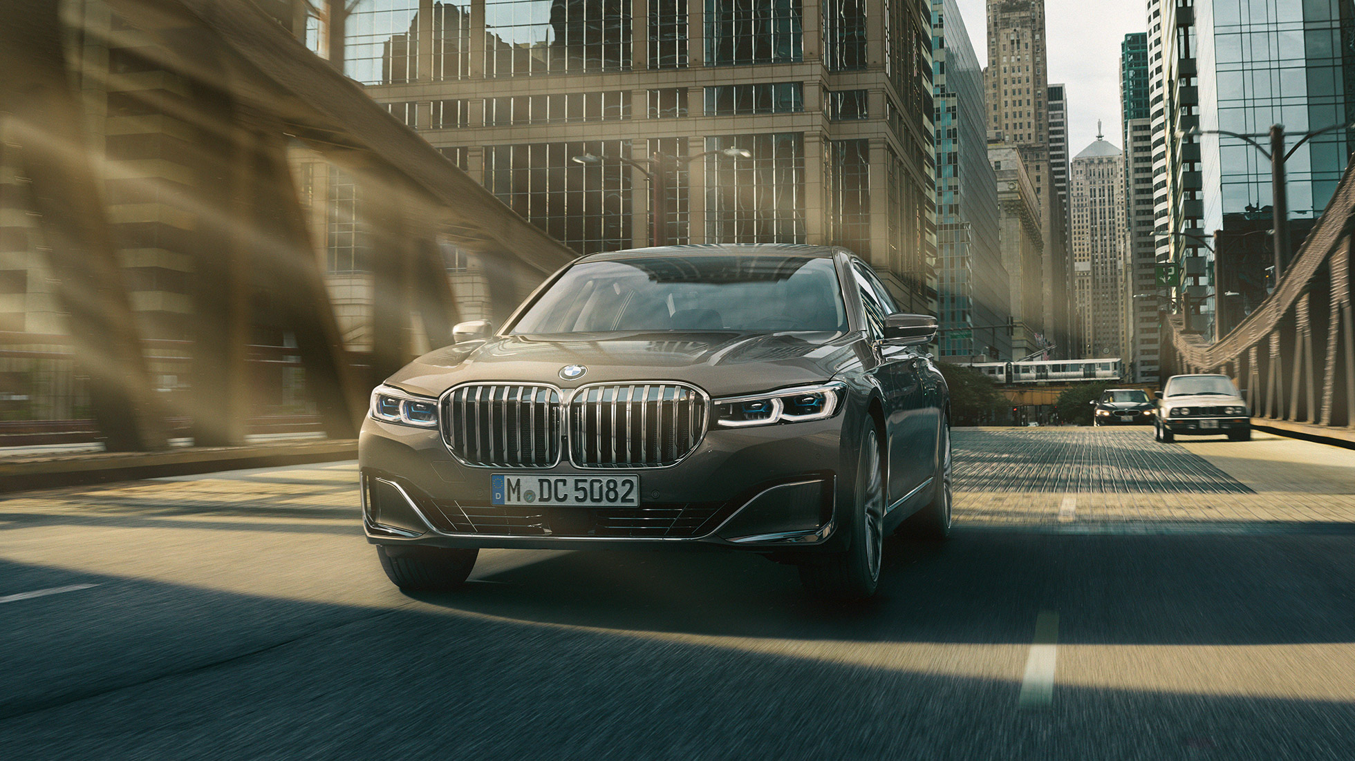 BMW 7 серии Седан: системы помощи водителю Системы помощи водителю: BMW 7 серии Седан в движении на фоне городского пейзажа