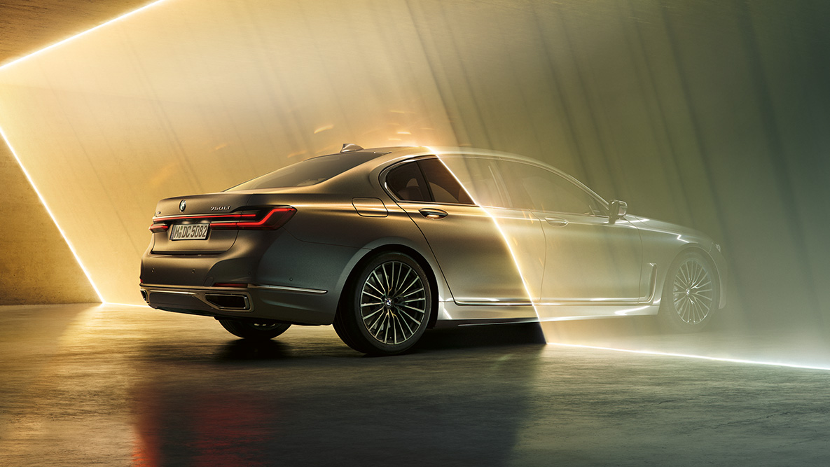 BMW 7 серии Седан цвета «Bernina Grey» BMW 7 серии Седан: автомобиль цвета «Bernina Grey», вид сзади с поворотом в три четверти в окружении потоков света