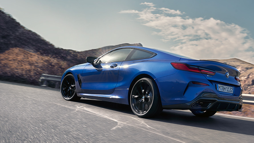 BMW 8 серии Coupé G15 LCI (рестайлинг 2022 года) в цвете Синий Портимау металлик, вид сзади с поворотом в три четверти, в движении на фоне холмов