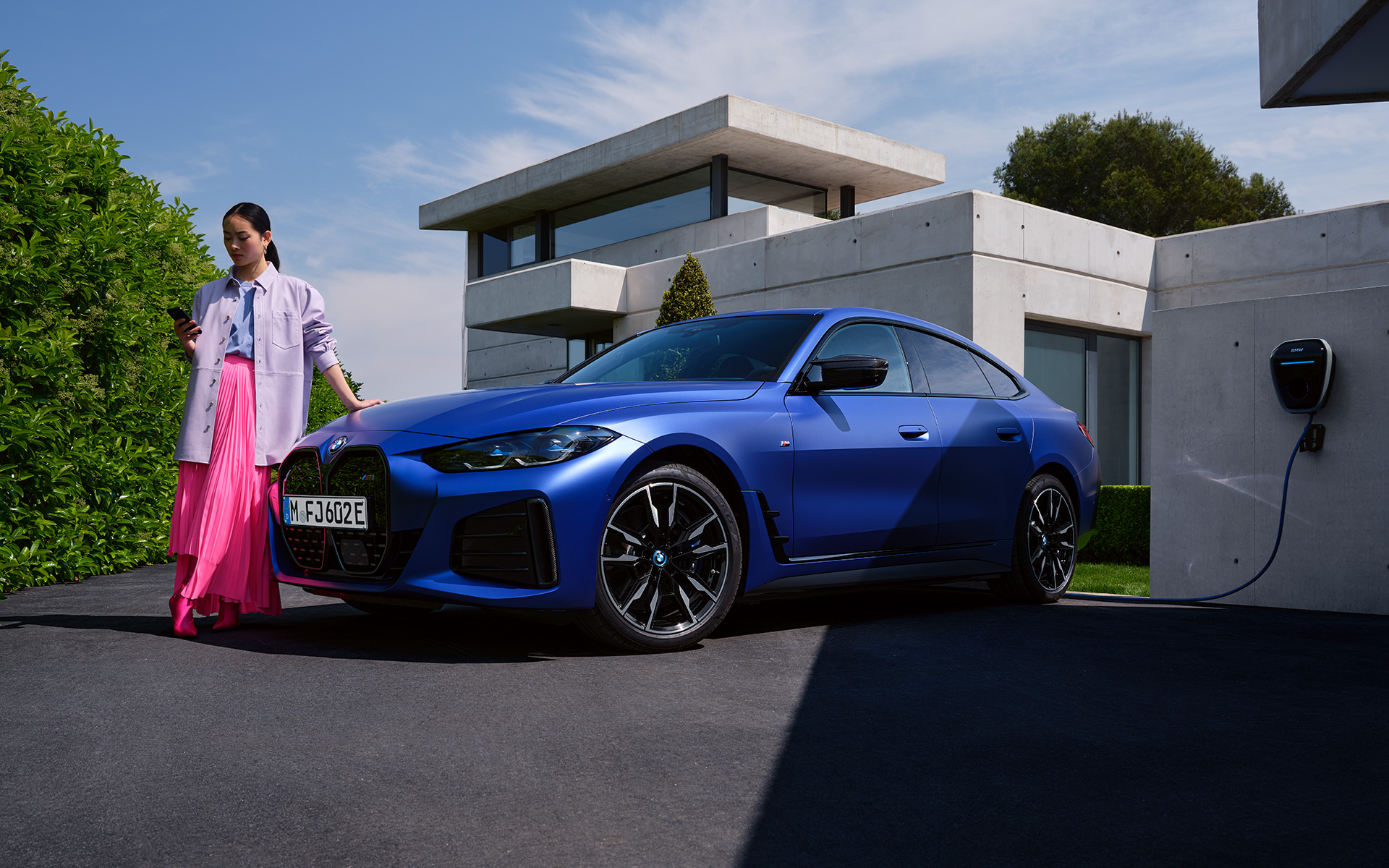 BMW i4 M50 G26 2021 &quot;Морозный Синий Портимау металлик&quot; BMW Individual, вид спереди в три четверти с женщиной перед домом