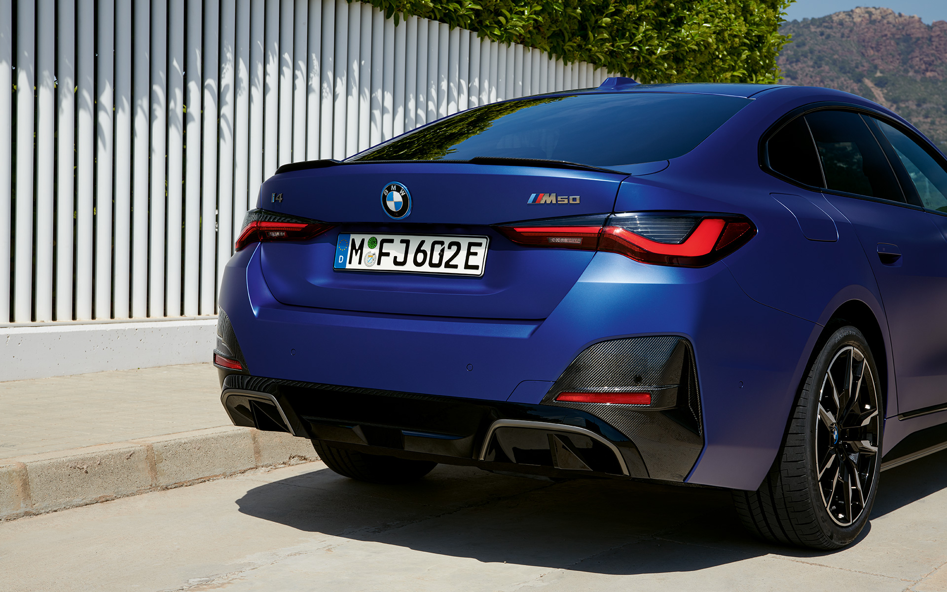 BMW i4 M50 G26 2021 &quot;Морозный Синий Портимау металлик&quot; BMW Individual, вид сзади в три четверти в статике у белого ограждения