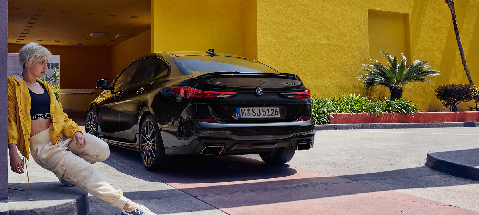 BMW M235i xDrive Gran Coupé вид сзади с поворотом в три четверти BMW M235i xDrive Gran Coupé Black Sapphire металлик F44 вид сзади с поворотом в три четверти с женщиной впереди