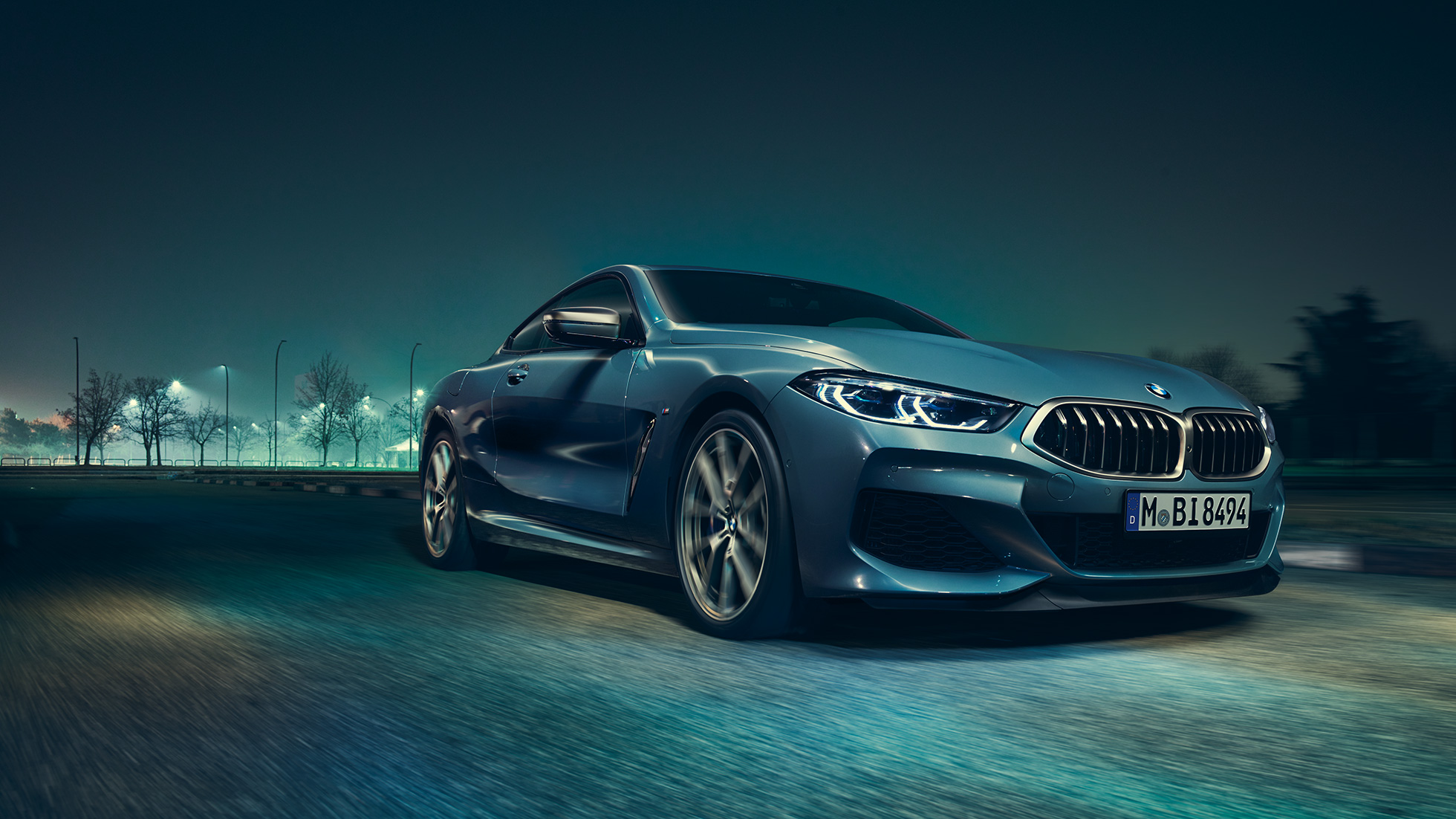 BMW M850i xDrive Coupé, вид спереди с поворотом в три четверти слева. BMW M850i xDrive Coupé в Barcelona Blue металлик, вид спереди с поворотом в три четверти слева, езда ночью.