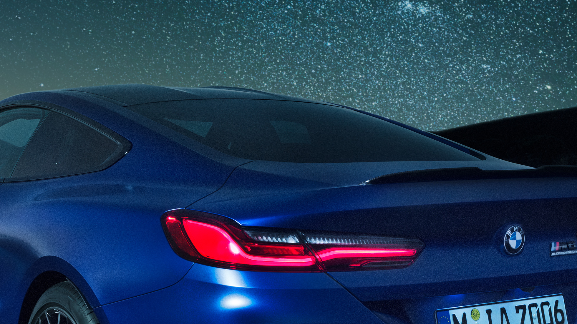 Задний спойлер М BMW M8 Competition Coupé в Marina Bay Blue металлик, ночная съемка плечевой части с задним спойлером M в карбоне.