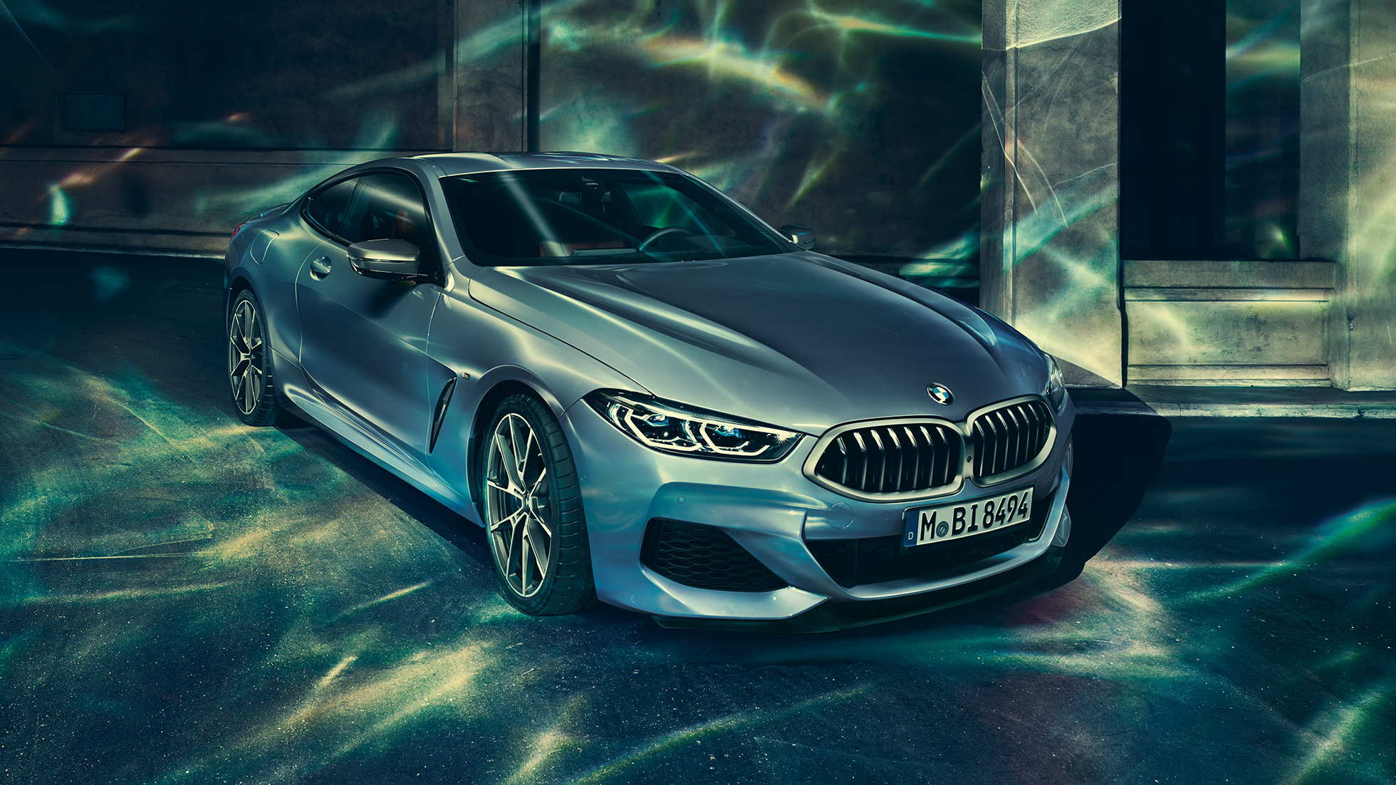 BMW M850i xDrive Coupé, вид спереди с поворотом в три четверти слева. BMW M850i xDrive Coupé в Barcelona Blue металлик, вид спереди с поворотом в три четверти слева, стоит перед зданием.