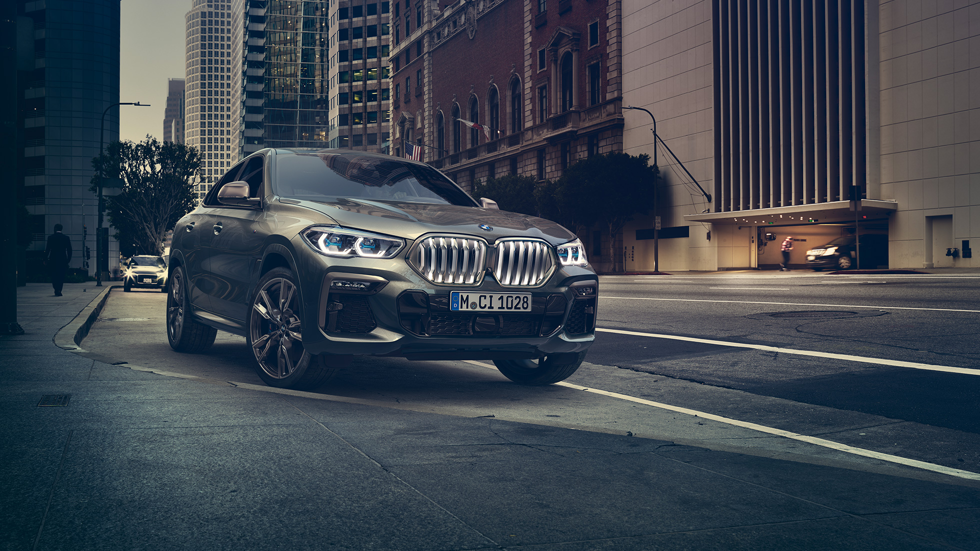 Неподвижно стоящий BMW X6 M50i BMW X6 M50i: вид спереди с поворотом в три четверти на фоне городского пейзажа