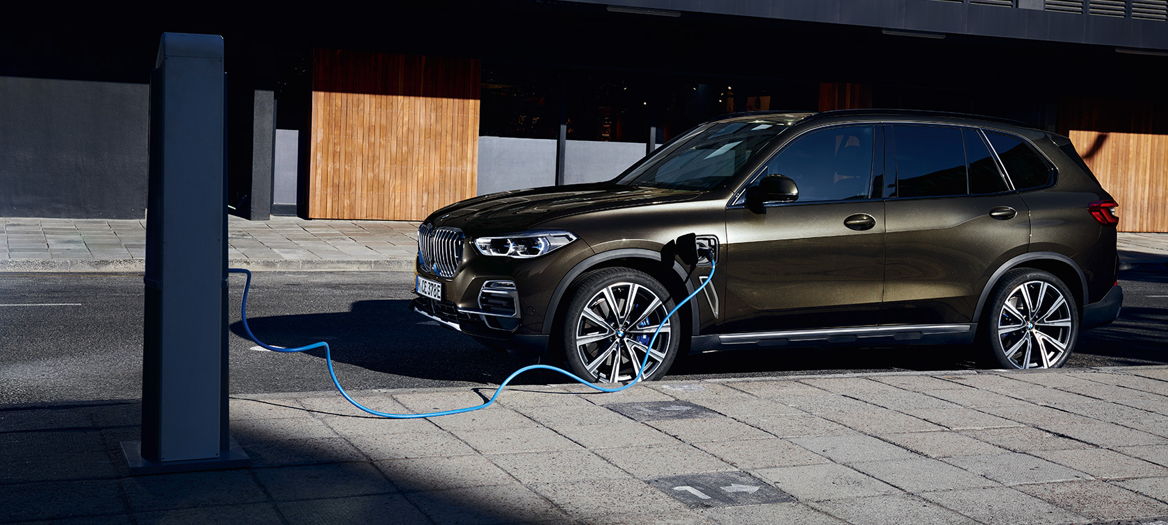 Плагин-гибрид BMW X5 xDrive45e G05, вид сбоку на три четверти Плагин-гибрид BMW X5 xDrive45e G05, вид сбоку на три четверти при зарядке